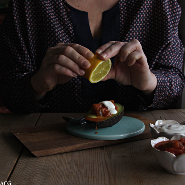 Bilde av ei som skviser sitronsaft over en halv avokado med salsa og rømme
